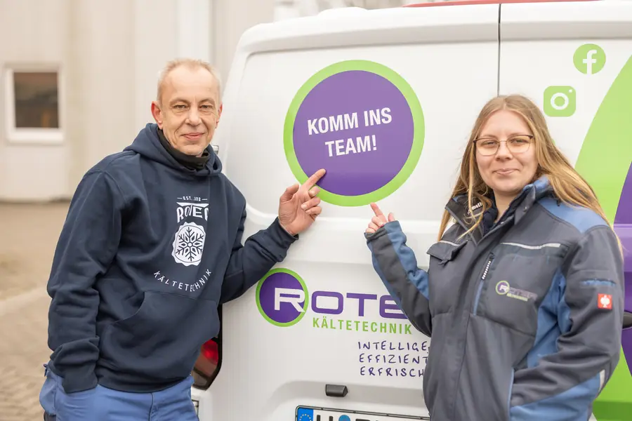 Kim und ein Kollege zeigen auf einen Servicewagen von Roter mit der Aufschrift „Komm ins Team!“